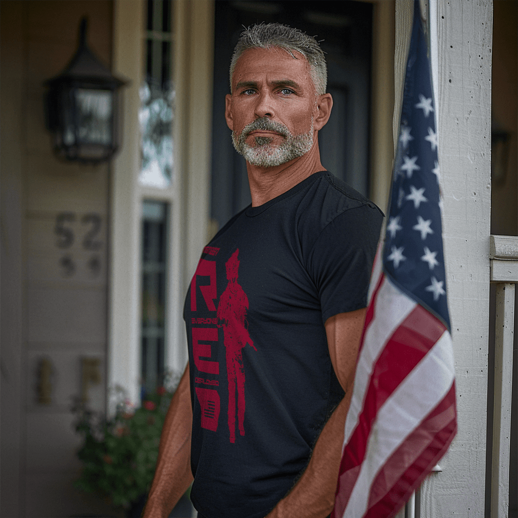 Middle-aged man on a porch, near an American flag, wearing a black t-shirt with red R.E.D. graphic and soldier silhouette.