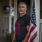 Middle-aged man on a porch, near an American flag, wearing a black t-shirt with red R.E.D. graphic and soldier silhouette.