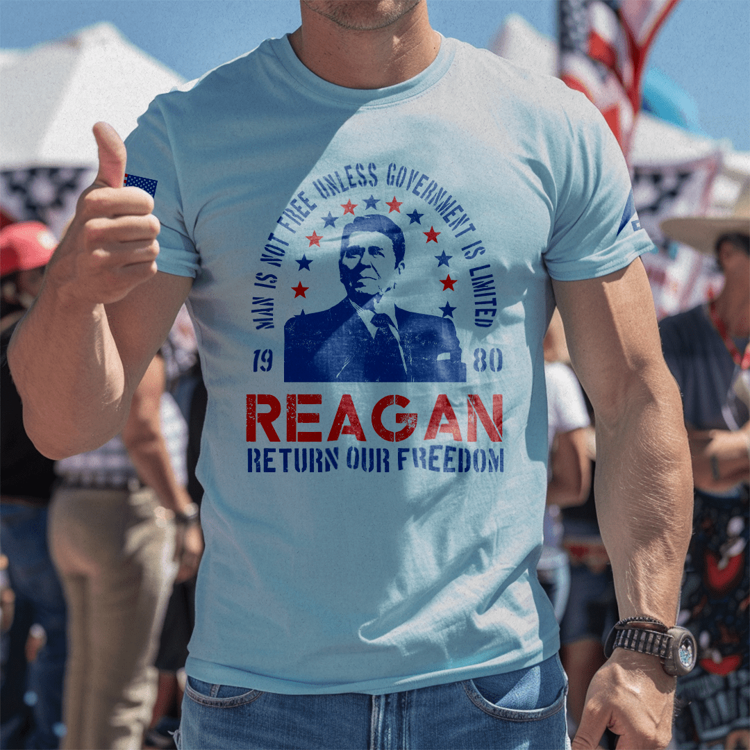 Man at an outdoor event giving a thumbs up while wearing a white Ronald Reagan t-shirt.