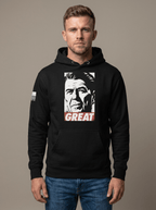 Man in studio wearing black hoodie featuring Ronald Reagan portrait graphic with "GREAT" text and American flag sleeve patch.