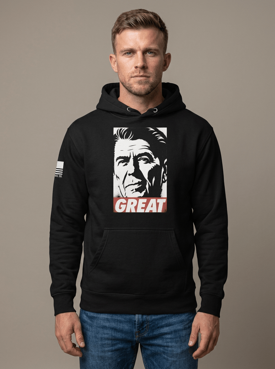 Man in studio wearing black hoodie featuring Ronald Reagan portrait graphic with "GREAT" text and American flag sleeve patch.