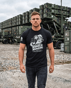 Man at military site wearing black t-shirt with cartoon Ronald Reagan on a missile graphic and "Peace Through Strength".