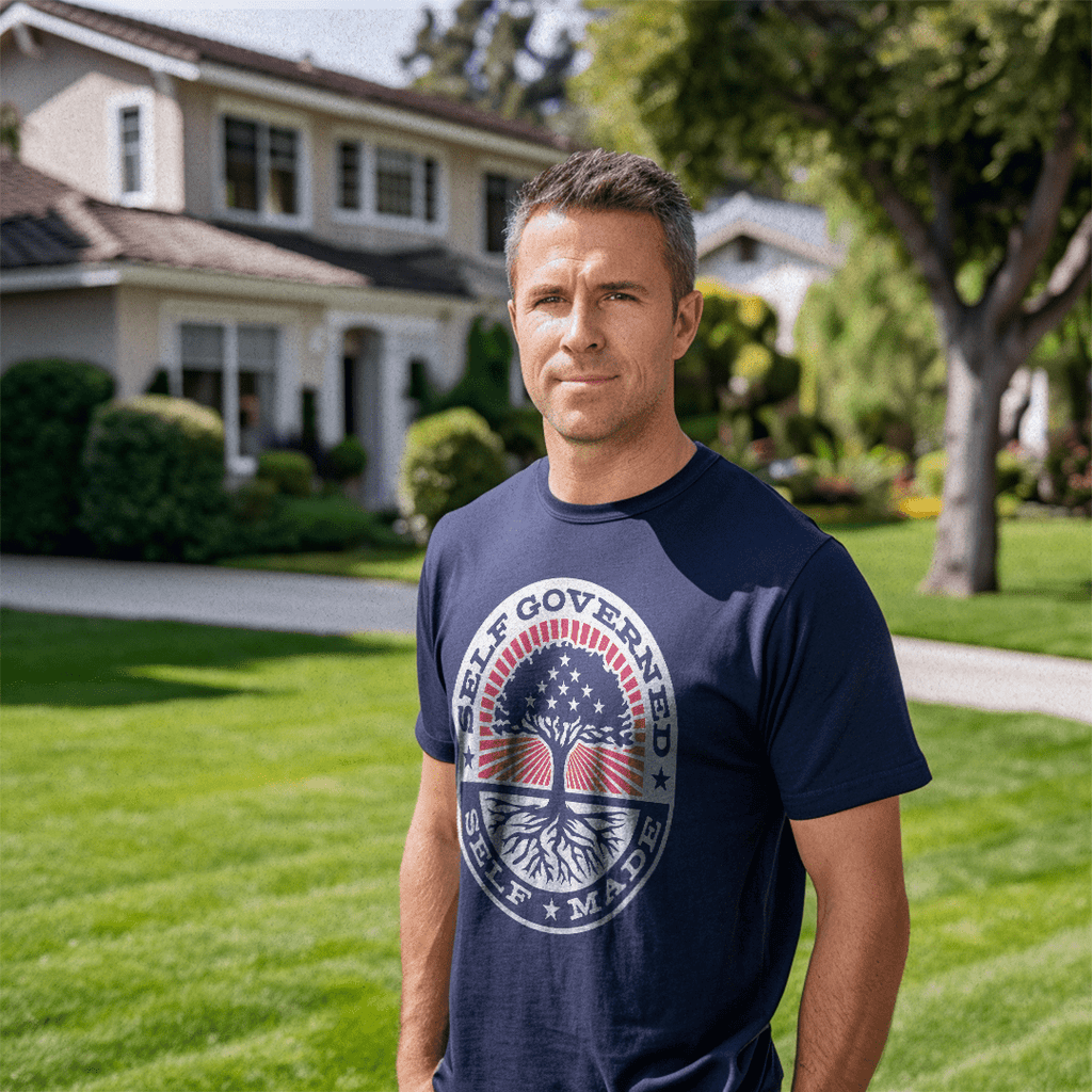 Man in a suburban yard wearing a navy Self Governed Self Made t-shirt with a flag-themed tree graphic and DIA logo.