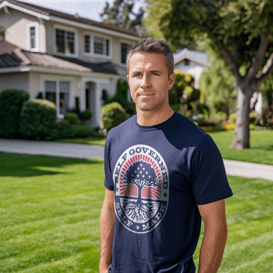 Man in a suburban yard wearing a navy Self Governed Self Made t-shirt with a flag-themed tree graphic and DIA logo.
