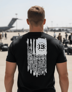 Man at an airfield wearing a black shirt with a distressed white American flag back graphic listing fallen names.