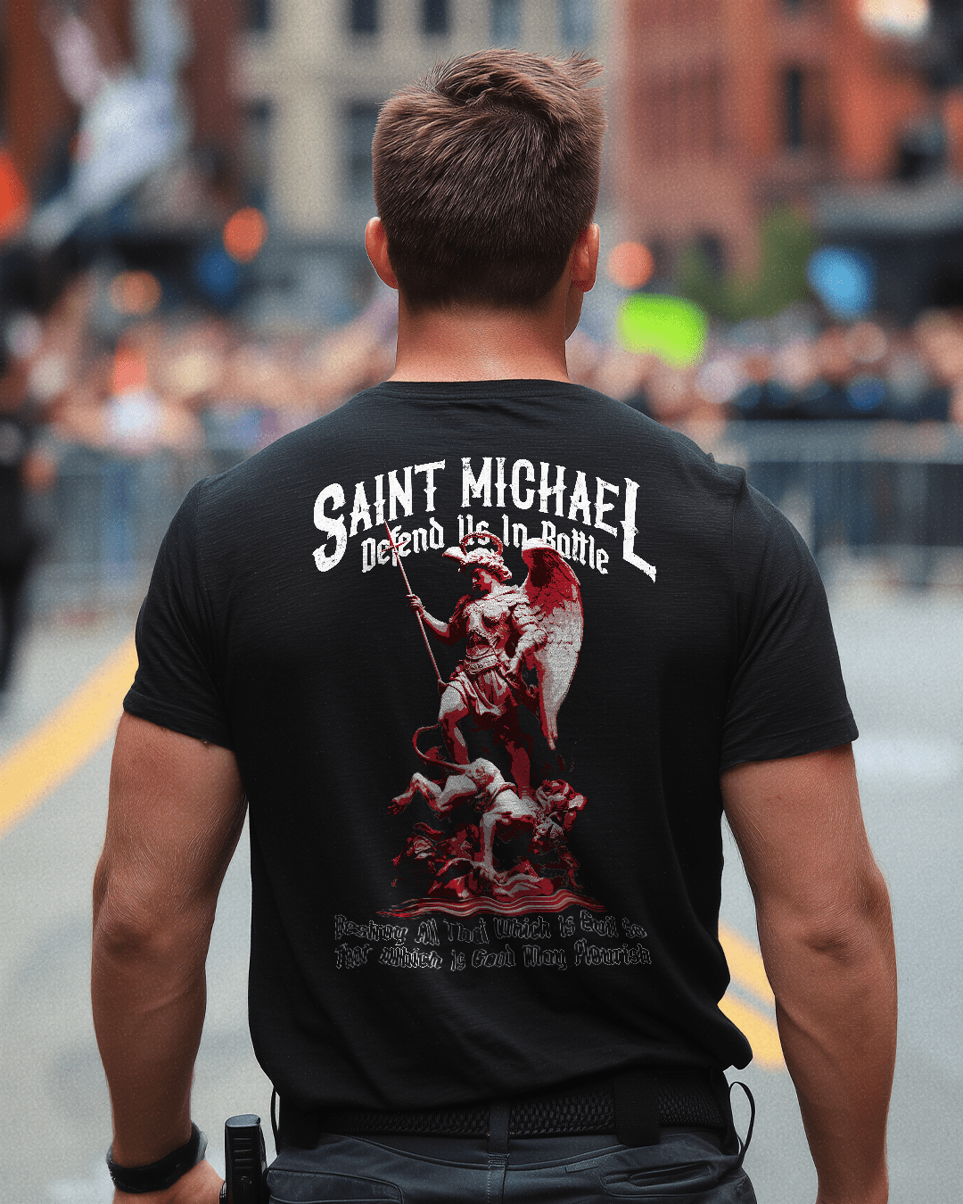Man standing in a city street, wearing a black t-shirt with a red and white Saint Michael graphic on the back.