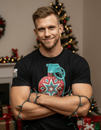 Man with blonde hair by a Christmas tree wearing a black t-shirt with a red grenade ornament graphic.