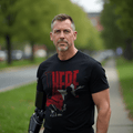 Man with prosthetic arm wears black t-shirt with "THERE" text, a map of Afghanistan, and an American flag on the sleeve.