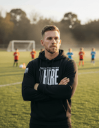 Man on a soccer field, wearing a black hoodie with "THERE" and "THANK YOU FOR YOUR SERVICE OVER THERE".