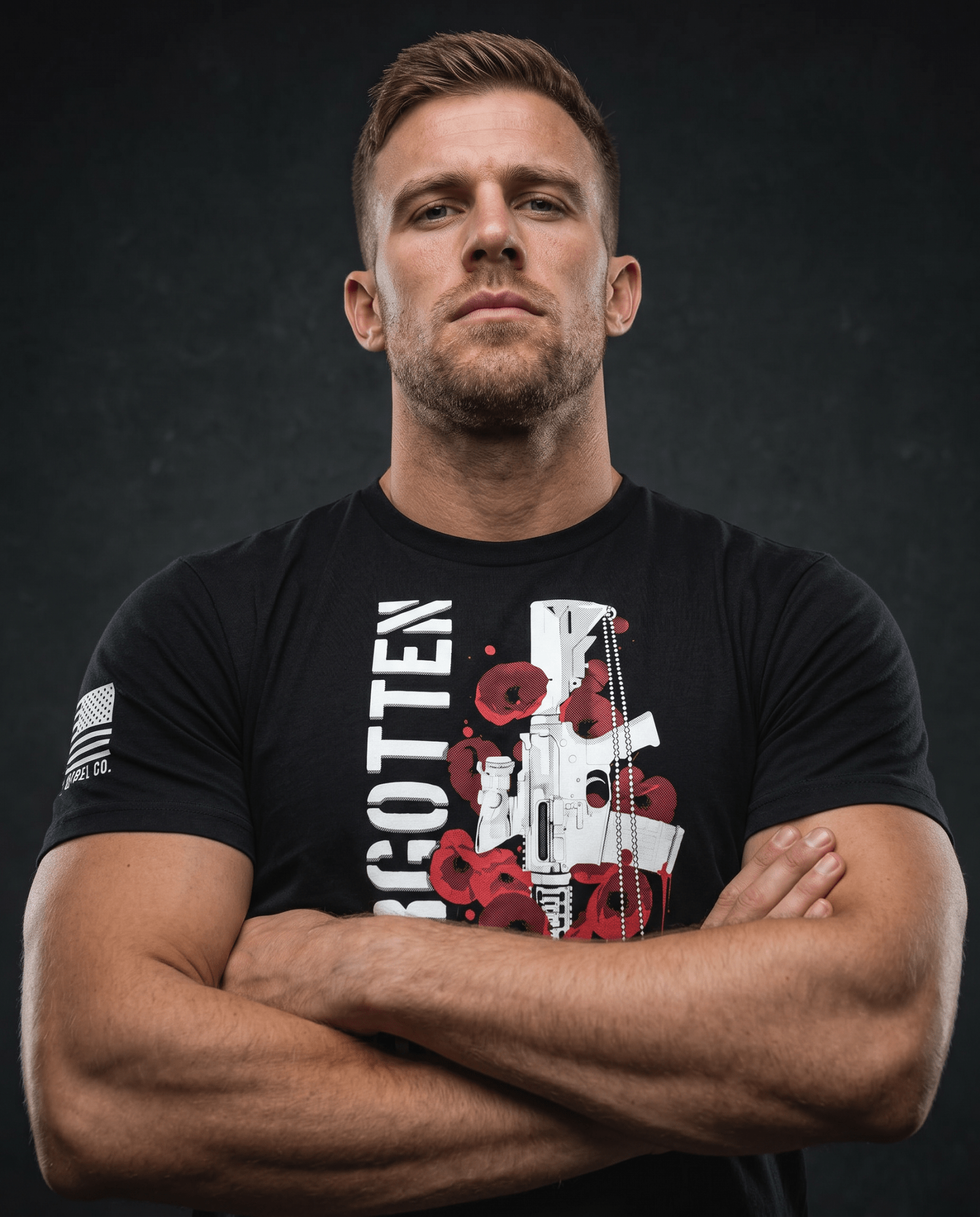 Man with crossed arms against a dark grey background, wearing a black t-shirt with a rifle and poppy graphic.