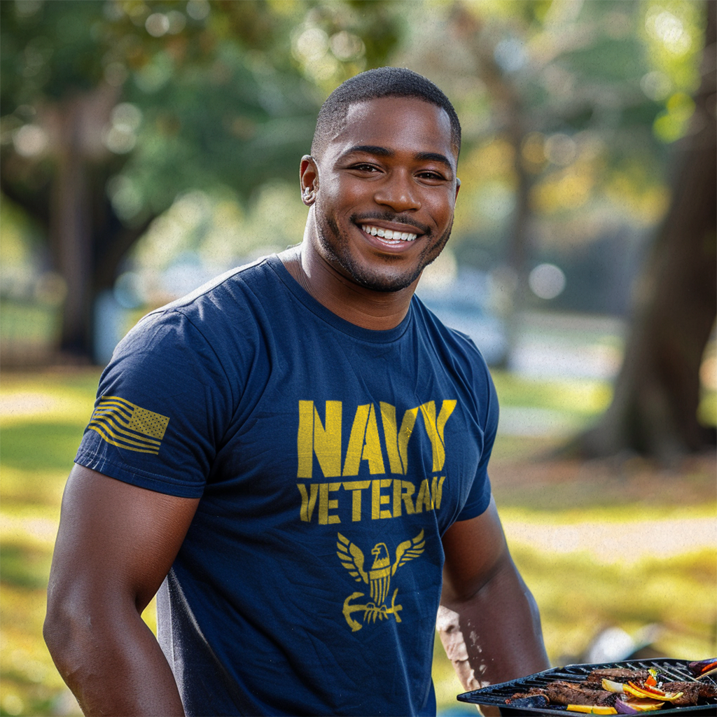 A man at a grill wearing a navy "NAVY VETERAN" t-shirt with an eagle emblem and American flag on the right sleeve.