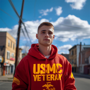 A man stands on a city street, wearing a red hoodie with a large yellow 'USMC Veteran' graphic, Marine Corps emblem, and a matching American flag and DIA logo on the sleeves.