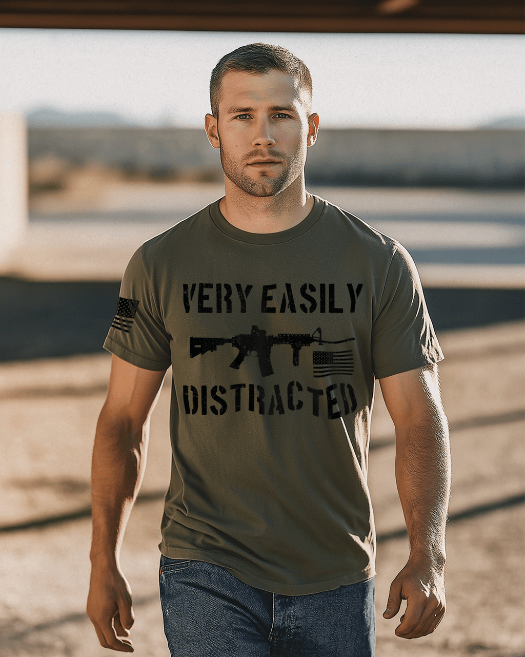 Man walking in a sunny area, army green shirt with black "VERY EASILY DISTRACTED" rifle graphic and an American flag.