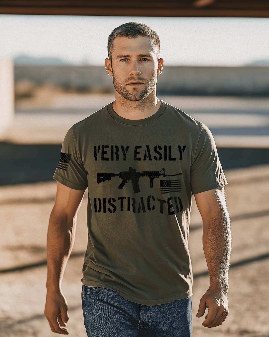 Man walking in a sunny area, army green shirt with black "VERY EASILY DISTRACTED" rifle graphic and an American flag.