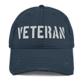 Navy blue distressed ball cap featuring "VETERAN" embroidered in white bold letters across the front crown.