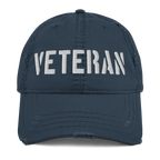 Navy blue distressed ball cap featuring "VETERAN" embroidered in white bold letters across the front crown.
