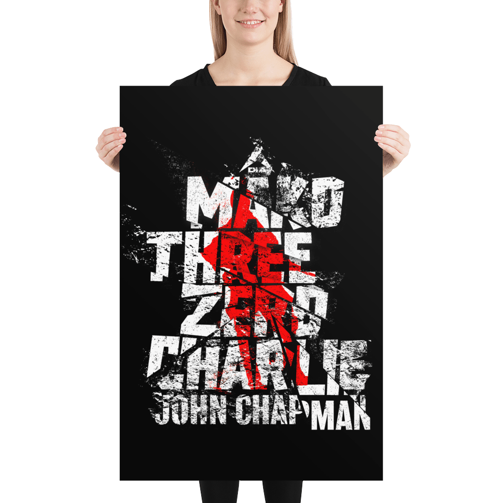 A woman holding a black poster featuring a distressed "Mako Three Zero Charlie" graphic in white and red.