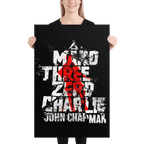 A woman holding a black poster featuring a distressed "Mako Three Zero Charlie" graphic in white and red.