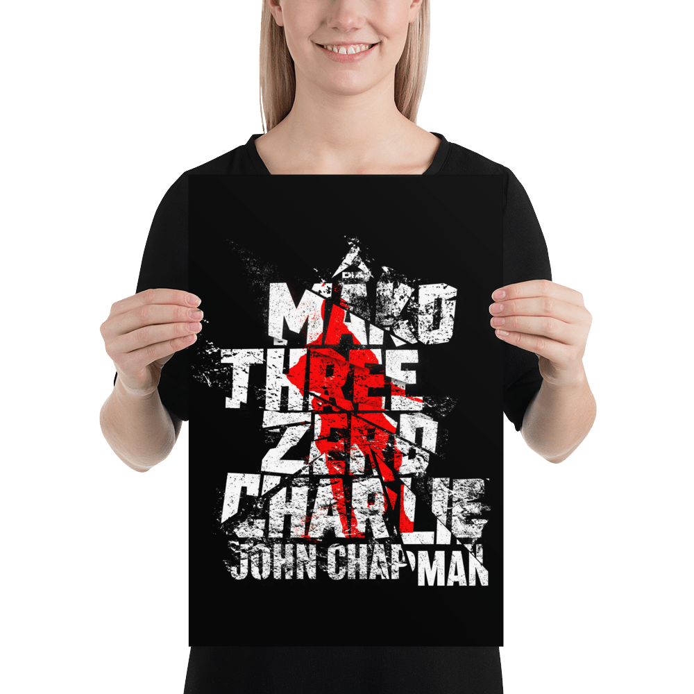 A smiling woman in a black shirt holds a poster with distressed "Mako Three Zero Charlie" text and a red graphic.
