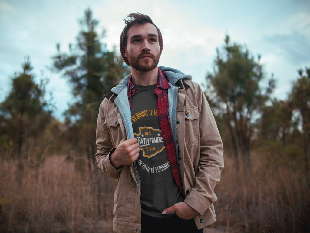man outdoors wearing a dark heather gray Pathfinder t-shirt under a tan jacket and red flannel shirt.